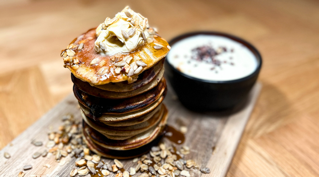 Stablede blåbær pandekager med smørklatten og granola, serveret med yoghurt og chiafrø, præsenteret på et træskærebræt - Danish Granola Company.