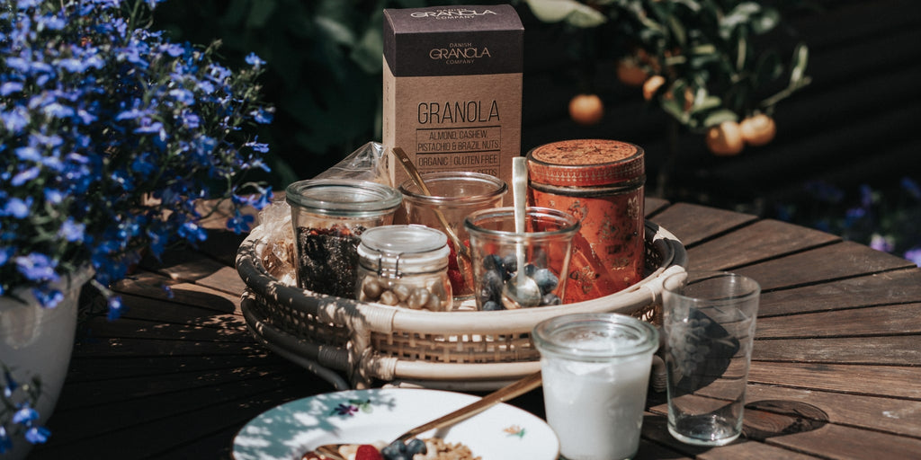 Danish Granola Company nøddemix granola på bordet med mælk og en smoothie skål i det solrige vejr.