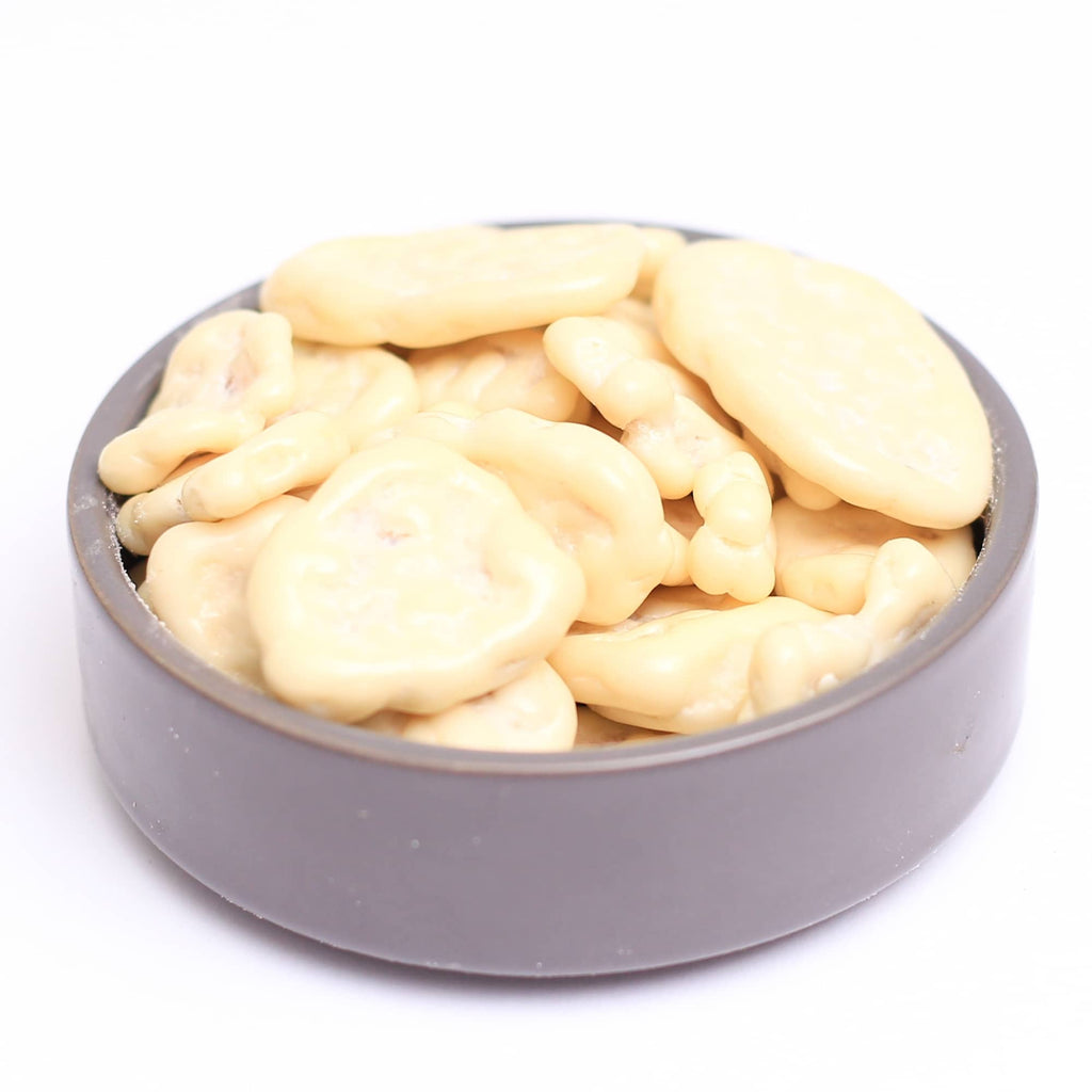 Bananchips overtrukket med hvid chokolade, foto med grå baggrund taget fra siden, med fokus på de chokoladebelagte chips.
